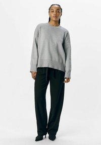 Grå oversized sweatshirt med ribbet nederkant og manchetter, parret med sorte wide-leg bukser og spidse sorte højhælede sko. Ensfarvet hvid baggrund.