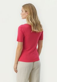 T-shirt aderente a maniche corte in cotone rosa brillante. Tessuto liscio, scollatura rotonda e design leggermente svasato. Abbinata a pantaloni di lino chiaro.
