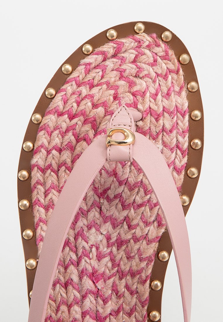 Vlechtstrooien sandalen met een roze en beige patroon, lichtroze banden, gouden accenten en een bruine zool met decoratieve studs langs de rand.