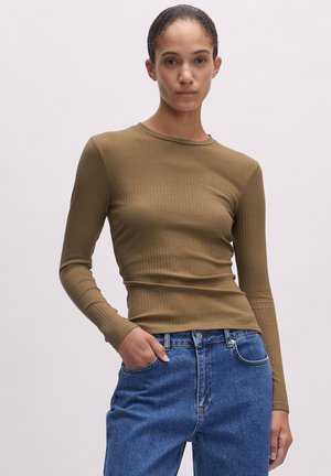 Olivgrünes, ribbeliges Langarmoberteil mit Rundhalsausschnitt. Kombiniert mit blauen Jeans aus Denim mit einer Fronttasche und Knopfverschluss.