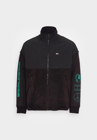 Černá bunda na zip s vysokým límcem. Vyznačuje se měkkou texturou, kontrastními matnými a lesklými materiály, tyrkysovým grafickým textem a emblémem.