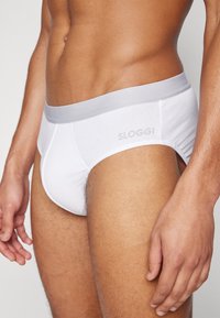 Weiße Baumwollslips mit einem grauen elastischen Bund, versehen mit dem dezenten Aufdruck des "SLOGGI" Logos. Glatte Textur, enganliegendes Design.