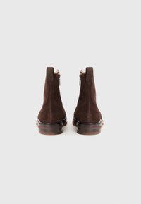 Stivaletti in suede marrone con suola in pelle liscia, dotati di una cerniera laterale e dettagli elastici per facilitare l'indossamento.