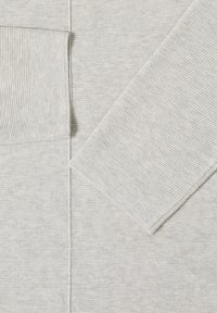 Tissu tricoté gris clair avec des textures côtelées et lisses formant un motif géométrique, incluant un détail de manche et de poche.