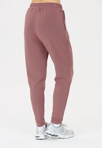 Lichtroze joggings met een elastische tailleband, zijzakken en een taperende pasvorm, gecombineerd met zilveren sportschoenen. Glad stoftextuur.