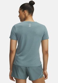 Camiseta atlética de manga corta en color teal con un acabado texturizado, que cuenta con un cuello redondeado y tres franjas verticales en la parte posterior.