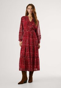 Röd blommig lång klänning med genomskinliga långa ärmar, V-ringning och lager-på-lager kjol. Styld med bruna klackboots. Mönstrad tyg med en lätt och flytande textur.