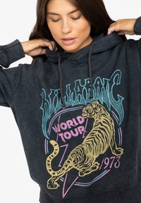 Čierna mikina s kapucňou s poškodenou textúrou látky, grafikou tigra a farebným dizajnom textu "World Tour". Kapucňa so šnúrkou a rebrované manžety.