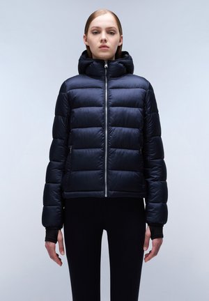Marineblauwe pufferjack met kap, voorzien van een rits aan de voorkant, een gewatteerd patroon en elastische manchetten, gedragen over zwarte leggings. Gladde textuur.