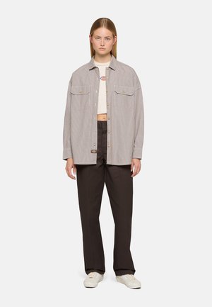 Camicia a righe con bottoni e due tasche frontali, abbinata a pantaloni scuri a vita alta. Il materiale sembra cotone, con una vestibilità comoda e tonalità neutre.