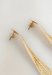 Zeltainas auskari ar viļņotu dizainu, ar teksturētu apdari un cilindriskām fiksējošām aizmugurēm drošai valkāšanai.