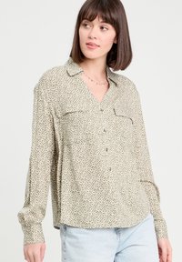 Long-sleeve, button-up shirt in olive green featuring a geometric pattern, two front pockets, and a collared neckline. Soft fabric texture.