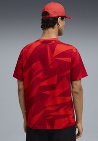 Rode T-shirt met korte mouwen, voorzien van een geometrisch patroon in verschillende tinten, gemaakt van katoen. De achterkant toont een ronde halsontwerp.