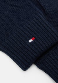 Guanti in maglia blu navy con polsini a costine e un piccolo logo rosso, bianco e blu sul lato. Texture morbida, realizzati in materiale di filato.