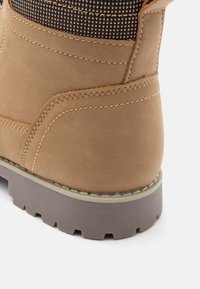 Brązowy skórzany but z teksturowanym czarnym panelem materiałowym, kontrastującymi szwami, grubą gumową podeszwą i wyściełanym kostką dla wygody.