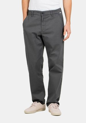 Grey cotton casual trousers with a relaxed fit, front pockets, and a button closure. Styled with light-colored sneakers.