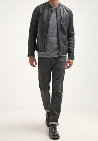 Černá kožená bomber bunda se zipem, šedý texturovaný svetr, tmavě šedé džíny a černé šněrovací boty. Model kráčející vpřed.