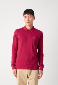 Langsleeve polo in dieprood katoen met een drie-knopen knoopsluiting en een logo-label aan de voorkant. Eenvoudig ontwerp met ribgebreide manchetten en kraag.