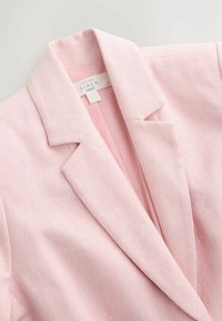 Blazer en lin rose doux avec col à revers cranté et texture subtile en chevrons, montrant une étiquette intérieure indiquant "Contient du lin NEXT."