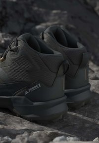 Ζευγάρι σκούρα γκρι παπούτσια πεζοπορίας Terrex που ακουμπούν σε πετρώδες έδαφος, δείχνοντας υφή στην επιφάνεια και παχιά σόλα.