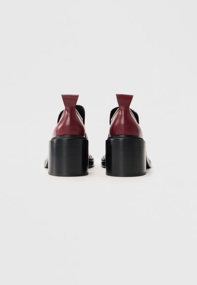 Pár bordových kožených botiček na podpatku s širokými černými blokovými podpatky, viděno ze zadní strany na bílém pozadí.