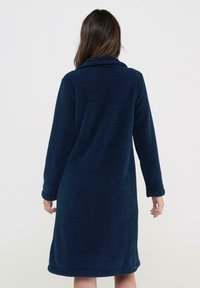 Bata de felpa azul marino con mangas largas, cuello y diseño hasta la rodilla. Tejido texturizado con un acabado suave y puños enrollados.