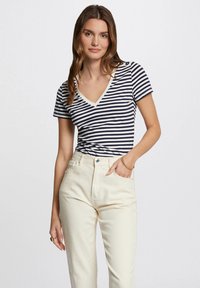 Marineblå og hvitstripet kortermet V-hals topp med beige kant, kombinert med høy midje kremfargede jeans med frontknapplukking.