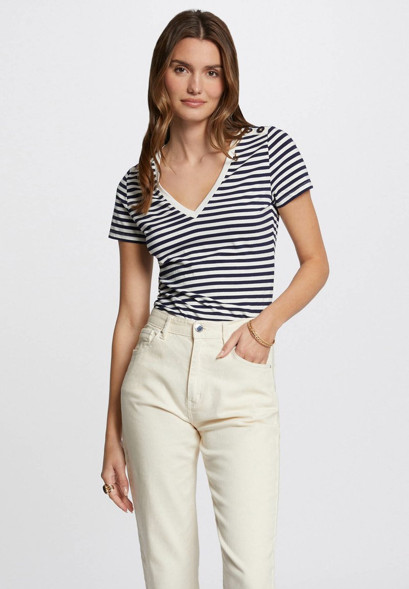 Marineblå og hvitstripet kortermet V-hals topp med beige kant, kombinert med høy midje kremfargede jeans med frontknapplukking.