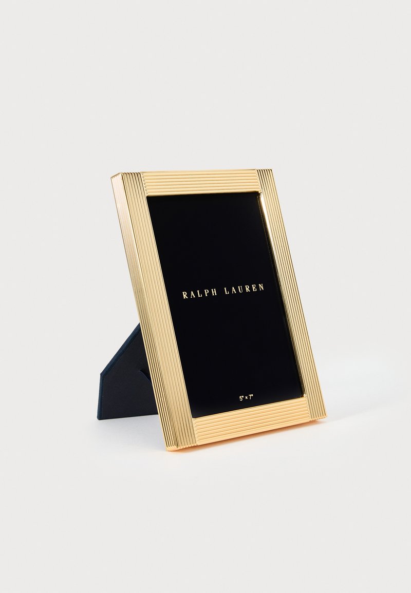 Arany bordázott képkeret fekete háttámlával és állvánnyal; "RALPH LAUREN" arany betűkkel jelenik meg rajta, 5"x7" méretű fényképekhez alkalmas.