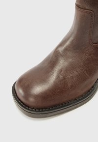 Bottine en cuir marron classique avec un bout rond, une texture lisse, de légères marques et des coutures renforcées le long de la semelle.