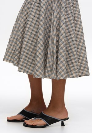 Piernas con sandalias negras de tacón bajo combinadas con una falda a cuadros gris y beige de longitud media.