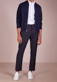 Námořnický zipový svetřík s vroubkovanými manžetami, kombinovaný s bílou košili s knoflíky a k ušitém tmavé kalhoty. Obuv tvoří bílé tenisky. Hladké textury.