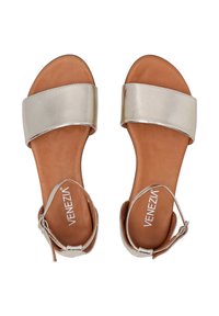 Metallisch silberne Sandalen mit einem breiten Vorderband und einem Knöchelriemen. Braune Leder-Innensohle. Verstellbarer Schnallenverschluss für einen sicheren Sitz. Flache Sohle.