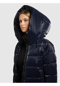 Mornarsko plava jakna s velikim, sjajnim kapuljačom, prošivenom teksturom i prednjim patentnim zatvaračem. Ima detalje sa špagom za stezanje i prilagođeni kroj.