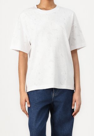 Bílý krátký rukáv tričko s texturovaným květinovým vzorem, volný střih, kulatý výstřih a měkká bavlněná látka. V kombinaci s modrými džíny.