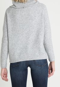 Grijs sweatervet met een hoge kraag, zachte textuur en raglanmouwen, gecombineerd met een donkere spijkerbroek met gedetailleerde achterstiksels.