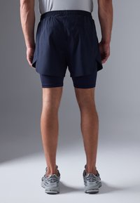 Şorturi atletice de culoare bleumarin, cu o croială lejeră, peste care sunt purtate șorturi de compresie bleumarin ajustate, având un talie elastică și slituri laterale.