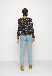 Top preto de mangas longas com flores pequenas multicoloridas, combinado com jeans de perna reta azuis claros e sapatos de salto em tom de bege.