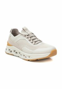 Zapatilla deportiva de color gris claro con parte superior de malla, acentos texturizados y una suela blanca acolchada, con una suela exterior de goma y diseño de cordones.