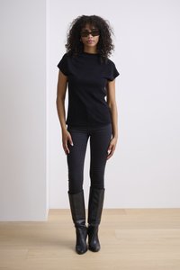 Haut noir à manches courtes associé à un jean skinny noir et des bottes en cuir noir jusqu'aux genoux. Des cheveux bouclés et des lunettes de soleil complètent le look.