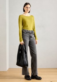 Langermet olivenfarget topp med rund hals, kombinert med grå jeans. Svart naglet belte, svart folderveske og kraftige svarte platåsko.