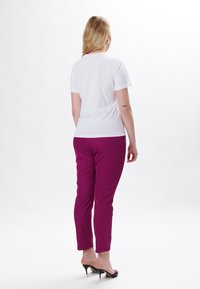 Hvid t-shirt, korte ærmer, parret med tætsiddende magenta bukser, glat tekstur og sorte åbne hæle, synlig ankel.