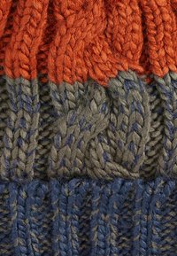 Gebreide beanie met afwisselende secties in oranje, grijs en blauw. Heeft een gestructureerd patroon met kabelbreiwerk en zachte vezels.