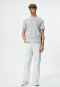 Lichtgrijze, getextureerde T-shirt met korte mouwen, gecombineerd met losse witte broek en witte sneakers, staand tegen een effen achtergrond.