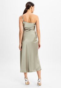 Eén-schouder, jurk tot halverwege de dij in zacht salie-groen satijn met plooidetails en een gestructureerde band. Gepaarde met zilveren sleehakken.
