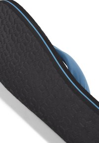 Suola in gomma nera con texture a nido d'ape, cinturini in tessuto blu e un accento bianco. Il design è resistente e adatto per un uso quotidiano.
