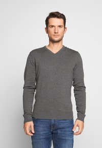Pulover gri cu guler în V, cu mâneci lungi, cu manșete și tiv cu nervuri, fabricat din material tricotat, purtat cu blugi albaștri. Design simplu și ajustat.