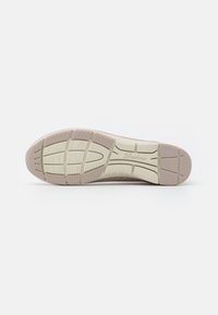 Shoe outsole with a textured light beige rubber surface, featuring a patterned grip and "Skechers" logo embossed.