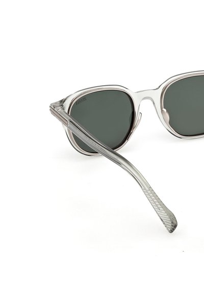 Okulary przeciwsłoneczne z przezroczystą oprawką, ciemnozielonymi soczewkami i teksturowanymi, srebrnymi zausznikami. Charakteryzują się smukłym, aerodynamicznym kształtem z zaokrąglonymi krawędziami.