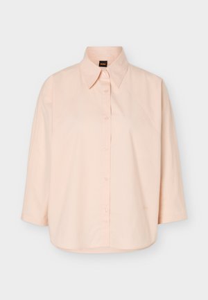 Ανοιχτό ροζ πουκάμισο με μακριά μανίκια, μυτερό γιακά και μαύρη ετικέτα με πορτοκαλί γράμματα "BOSS" μέσα στον γιακά.